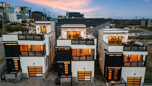 Un edificio residencial moderno de varios pisos con balcones, ventanas amplias y un camino de acceso.