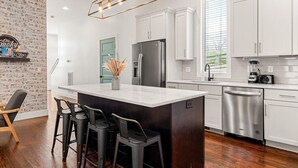 Una cocina moderna con armarios blancos, una isla central con taburetes de bar, un refrigerador de acero inoxidable y un lavavajillas integrado.