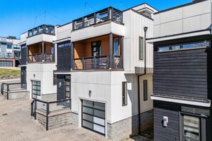 Un immeuble résidentiel moderne à plusieurs étages, doté de balcons, de grandes fenêtres et d’un rez-de-chaussée pavé de briques.