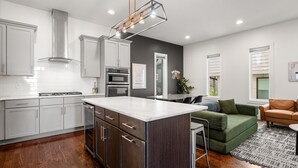 Une cuisine moderne avec des meubles blancs, un îlot central, des appareils en acier inoxydable et un luminaire suspendu.