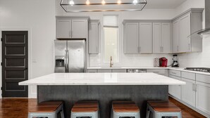 Une cuisine moderne dotée d’un grand îlot central, d’appareils électroménagers en acier inoxydable et d’un luminaire suspendu original.