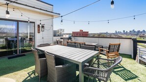 A rooftop patio with a table and chairs, string lights, and a view of the city skyline.