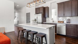 A modern kitchen with a central island, bar stools, dark wooden cabinets, stainless steel appliances, and a pendant light fixture.