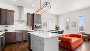 A modern kitchen with dark cabinets, a white island, and a dining area with a red sofa and a dining table.