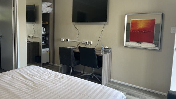 Habitación de hotel con cama, escritorio con silla, televisión y espejo con un cuadro.