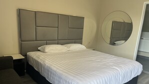 Una habitación de hotel moderna con una cama grande, una mesita de noche y un espejo redondo en la pared.