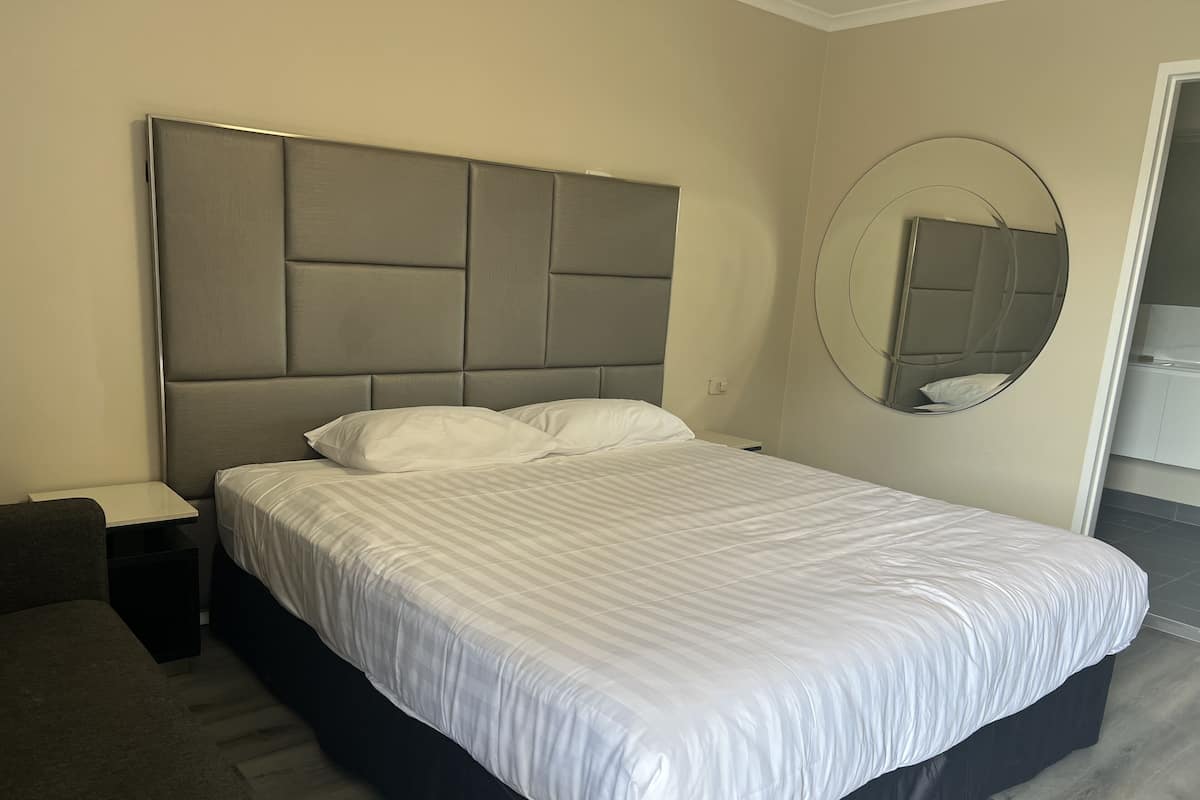 A modern hotel room with a large bed, a bedside table, and a round mirror on the wall.
