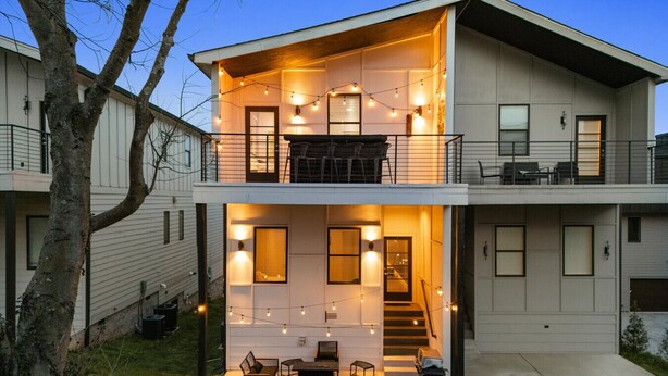 A two-story residential building with a balcony, outdoor seating area, and string lights.