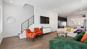 A modern living room with a staircase, a dining area, and a kitchen.