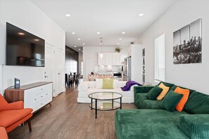 A modern living room with a green sofa, orange armchair, and a glass coffee table.