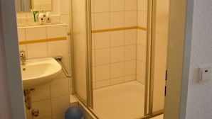Ein Badezimmer mit Dusche, Waschbecken und Toilette. Ein Paar Sandalen liegen auf einem Handtuch am Boden.