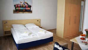 Ein Hotelzimmer mit einem Bett, einem Holzschrank, einem Bild an der Wand und einem Tisch mit Früchten und Blumen.