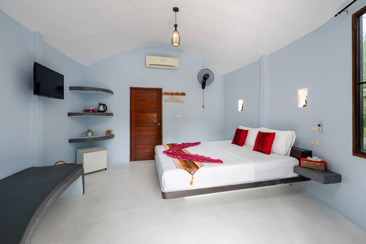 Een slaapkamer met een bed, een televisie, een ventilator, een verwarming en een raam.