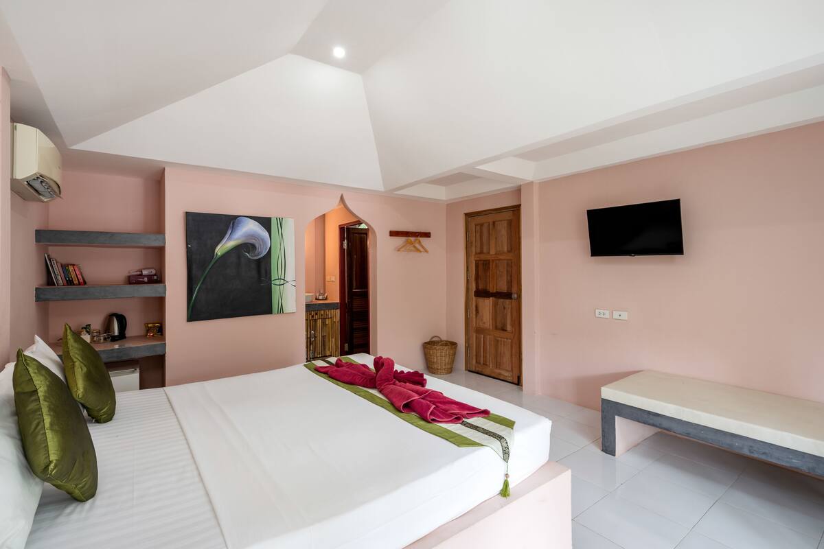Een slaapkamer met een bed, een bankje, een televisie en een schilderij aan de muur.
