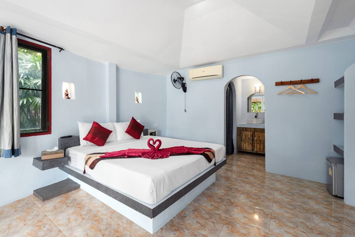 Een moderne slaapkamer met een groot bed, een nachtkastje, een kleine bedlamp, een wandairconditioner en een raam met gordijnen.