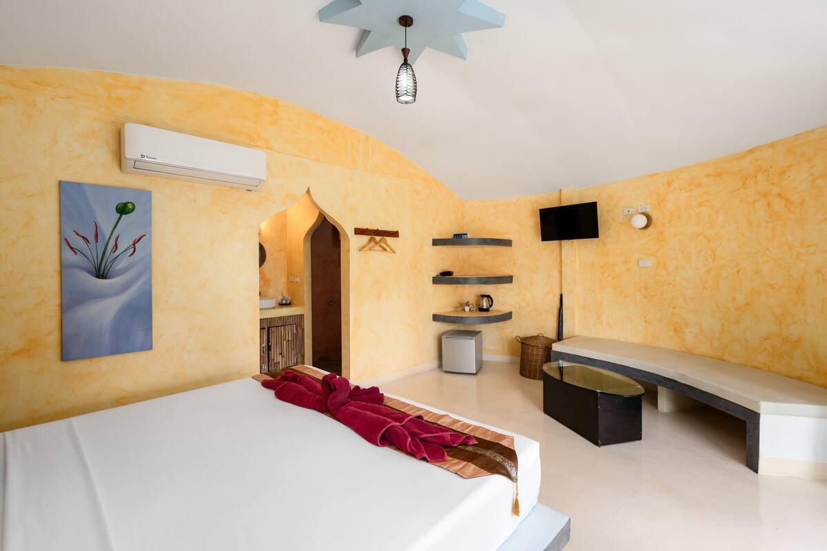 Een moderne slaapkamer met een bed, een bankje, een klein tafeltje, een aan de muur bevestigde televisie en een airconditioner.