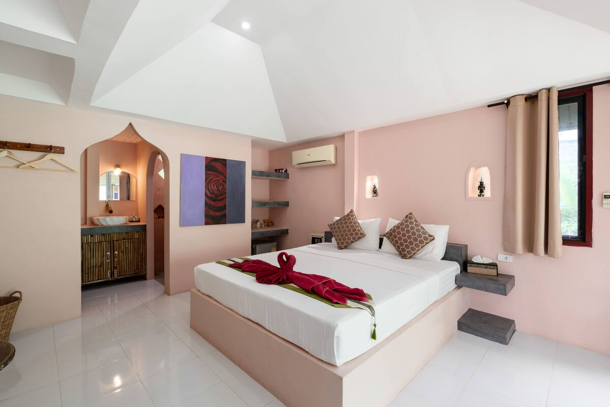 Ruime slaapkamer met een groot bed, een kaptafel met spiegel, en een badkamer zichtbaar door een boog.