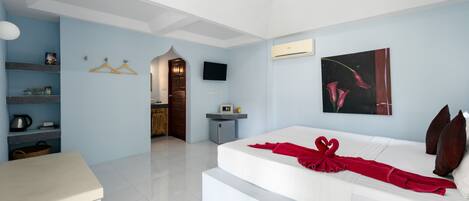 Una habitación de hotel moderna con una cama grande, un televisor de pantalla plana, un cuadro y una kitchenette.