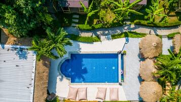 An aerial view of a resort with a swimming pool surrounded by palm trees and thatched umbrellas.