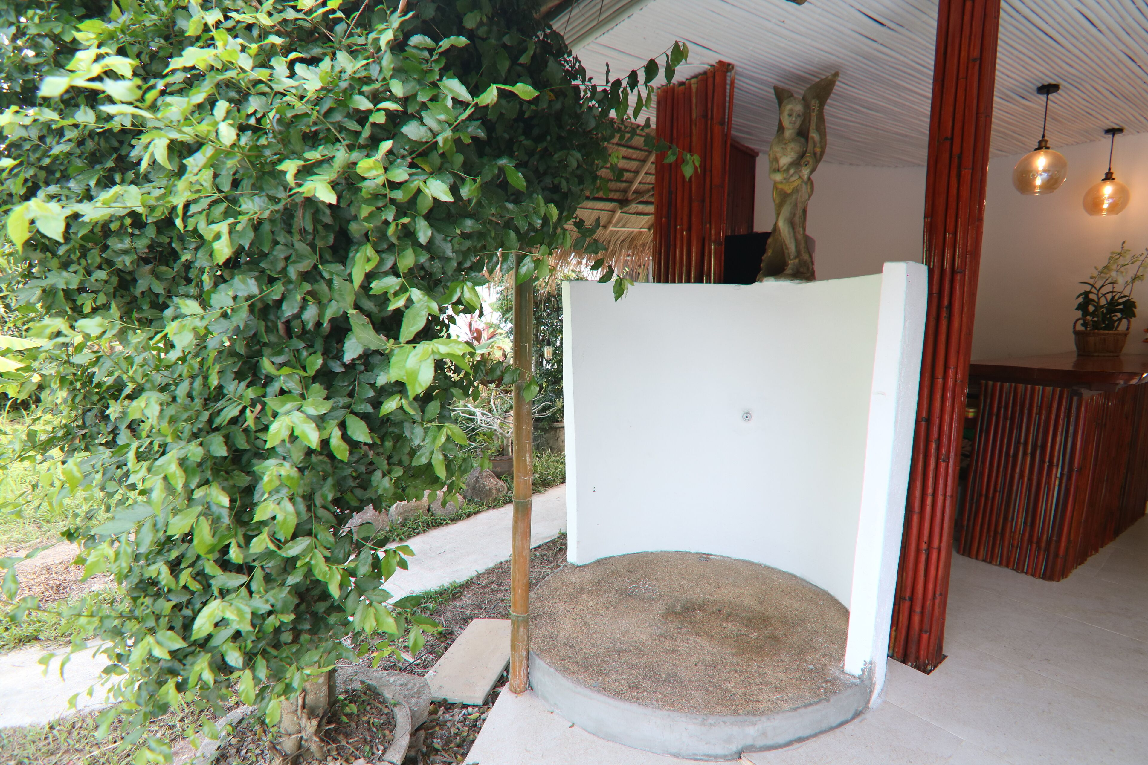 Quarto com parede branca, um espaço de estar pequeno e circular, e estrutura de bambu.