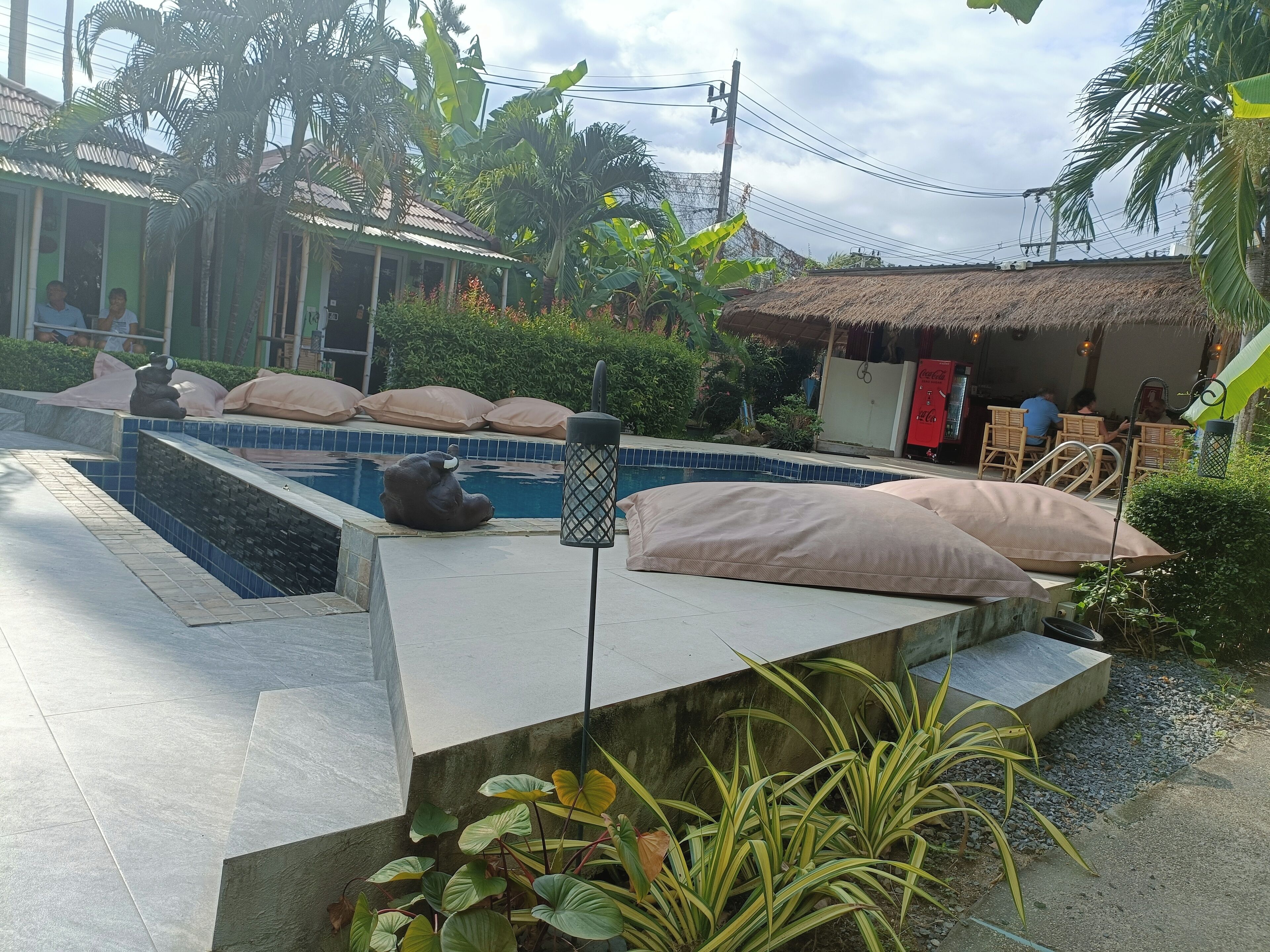 A pool area with a statue, a covered seating area, and a building in the background.