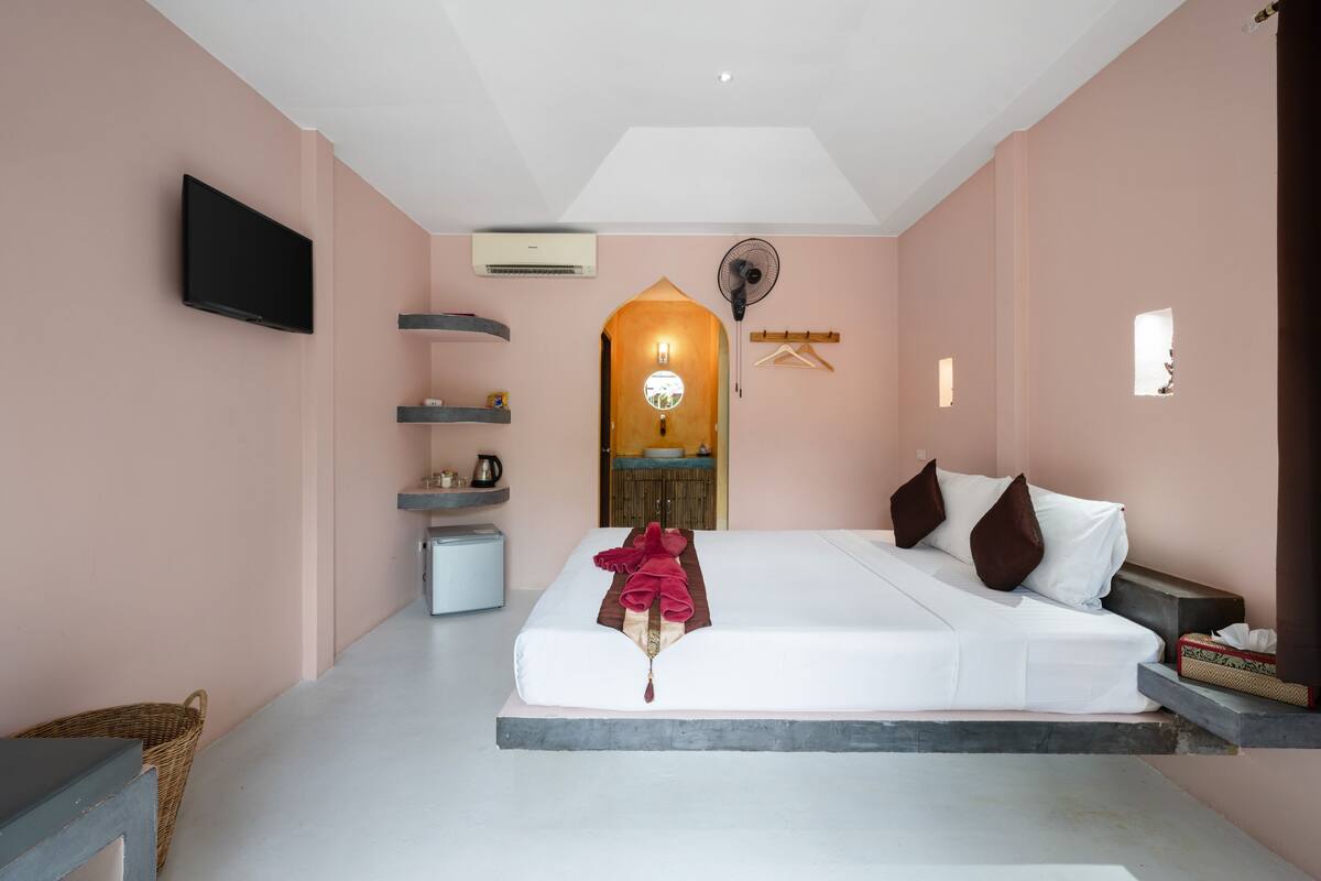 Een slaapkamer met een bed, een televisie, een ventilator en een klein tafeltje met een mand.