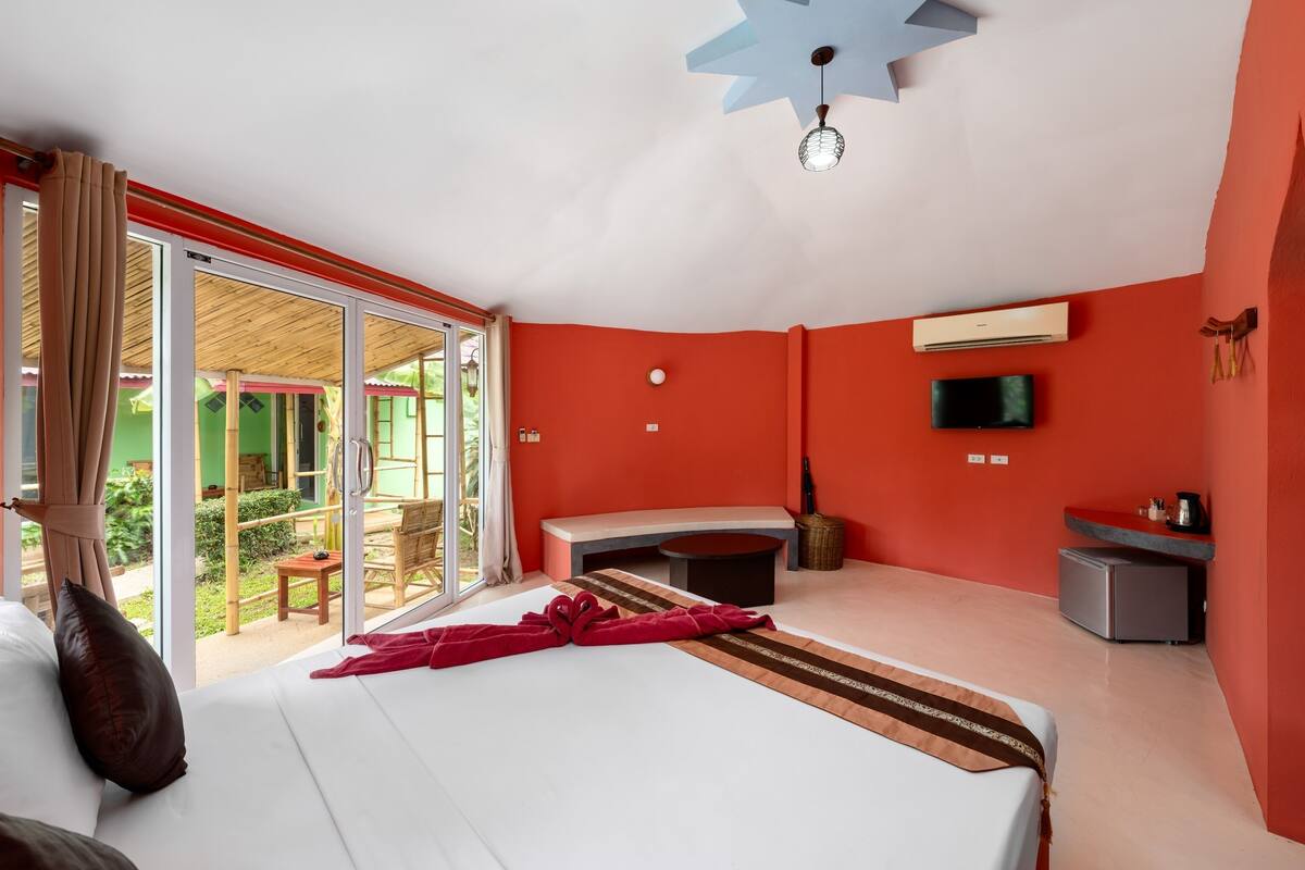 Een hotelkamer met een bed, een bureau, een televisie en een schuifglazen deur naar een terras.