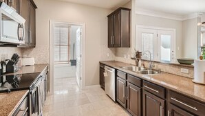 A modern kitchen with dark wooden cabinets, a stainless steel sink, and a granite countertop. - Warm Suburban 3BR Townhome near DT (Austin)