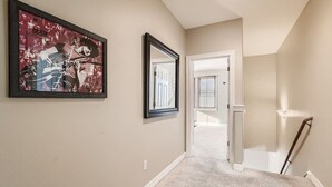 A hallway with a carpeted floor, a framed abstract painting, and a door leading to another room. - Warm Suburban 3BR Townhome near DT (Austin)
