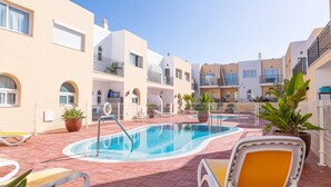 A pool area with lounge chairs, a swimming pool, and a building with balconies. - Townhouse in Palm-Mar  (Arona)