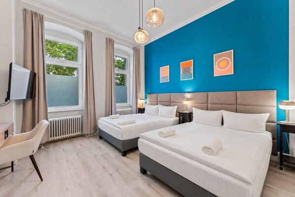 A hotel room with two beds, a desk, a chair, and a TV.