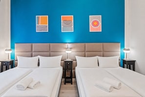 Camera d'albergo con due letti, una parete di colore blu e tre opere d'arte incorniciate.