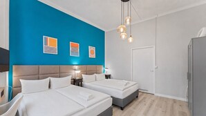 Une chambre d’hôtel avec deux lits, un bureau, une chaise, une armoire et un mur d’accent bleu agrémenté d’œuvres d’art.