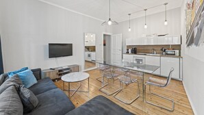 Un salon moderne avec un canapé, une table à manger en verre et des chaises transparentes. Il y a également un coin cuisine avec des meubles blancs et un four à micro-ondes.