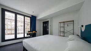 Et moderne hotelværelse med en stor seng, et skrivebord og udsigt til omgivelserne gennem store vinduer.