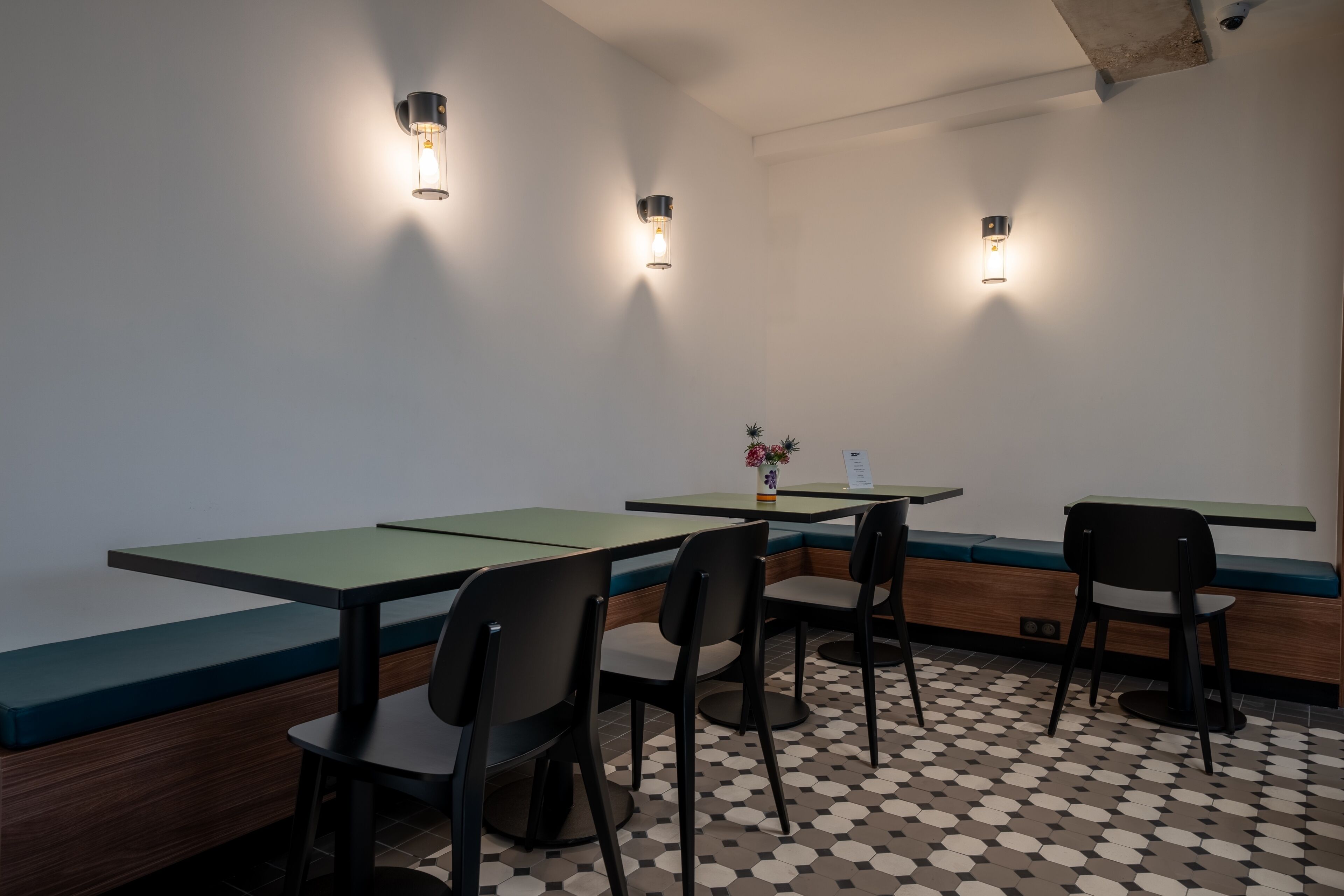 A modern dining area with green cushioned benches, black chairs, and a patterned floor.