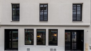 En bygning med flere etager og en symmetrisk facade, med jævnt placerede rektangulære vinduer og en central indgang med glasdøre.
