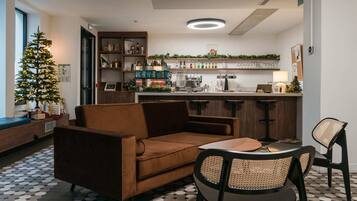 Un salon confortable avec un canapé, des fauteuils, une table basse, un petit sapin de Noël et un coin cuisine doté d’un comptoir-bar et d’étagères.