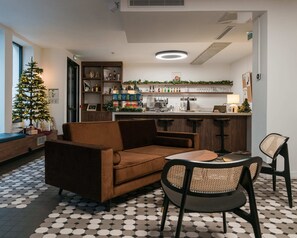 A cozy living area with a sofa, chairs, a coffee table, a small Christmas tree, and a kitchen area with a bar counter and shelves.