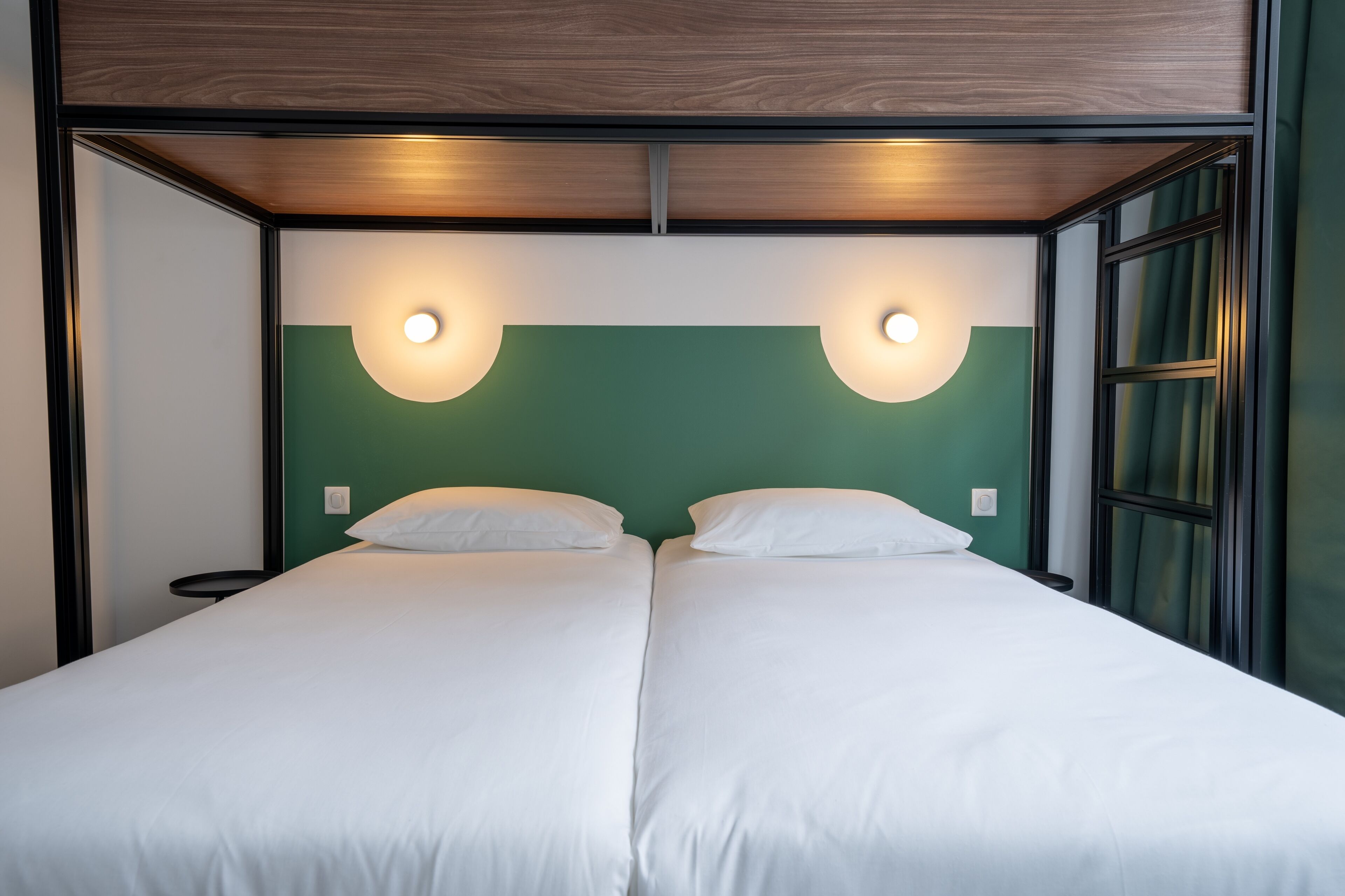 Un lit double avec du linge de lit blanc, deux lampes fixées au mur et un mur d’accent de couleur verte.
