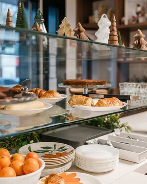 A buffet with various pastries and desserts, including croissants and a cake, displayed on glass shelves.