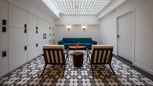 Et moderne interiør med et geometrisk gulvmønster, et rundt bord i midten, to lænestole, en blå sofa og et ovenlys.