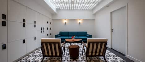 A modern interior with a geometric patterned floor, a central round table, two armchairs, a blue sofa, and a skylight above.