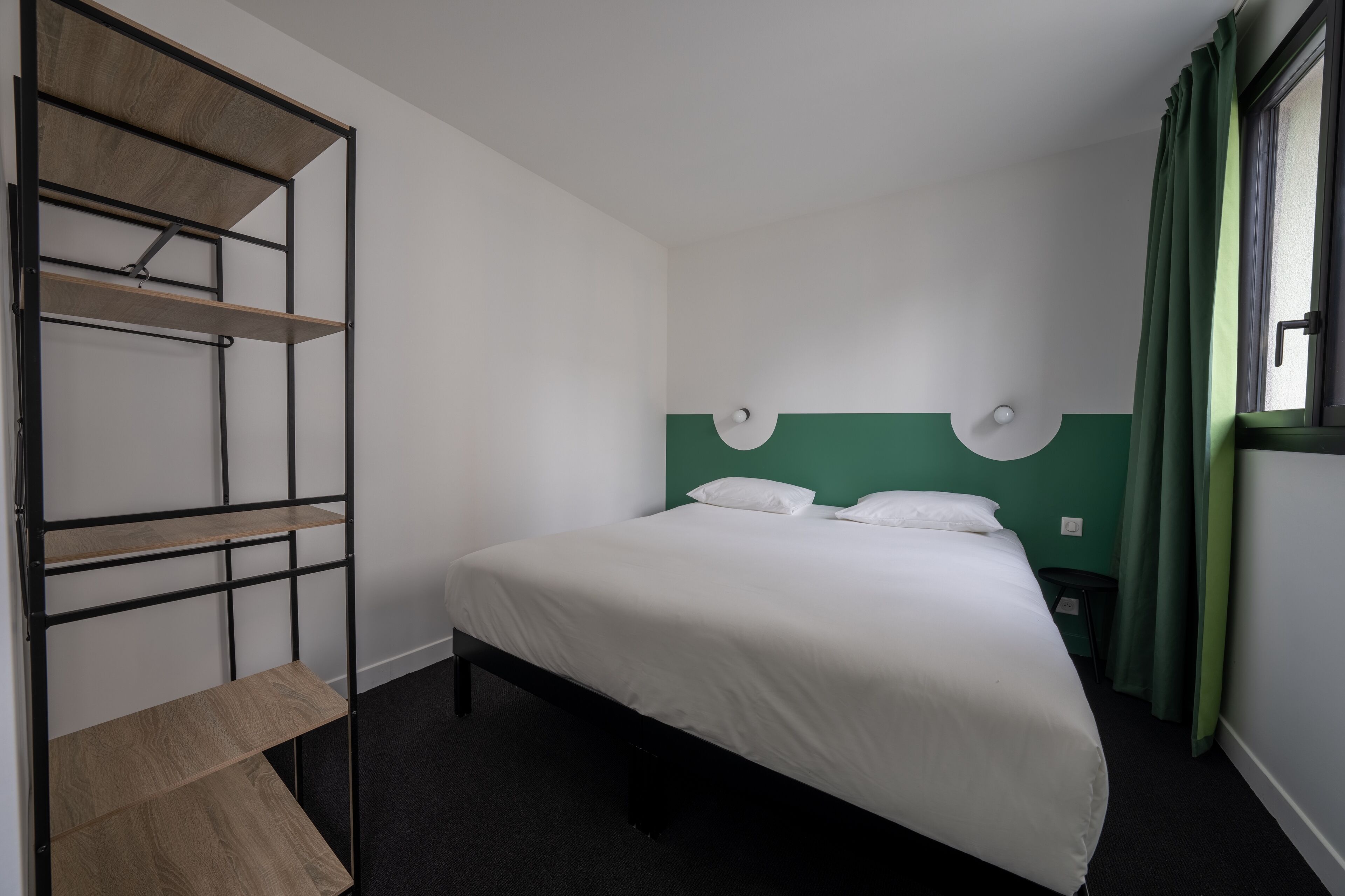 A hotel room with a bed, a wooden shelf unit, and a green accent wall.