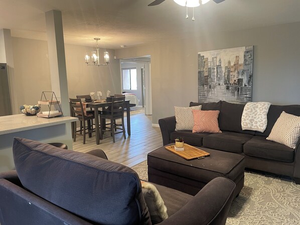A modern living room with a dark-colored sofa, a wooden coffee table, and a dining area with a table and chairs.