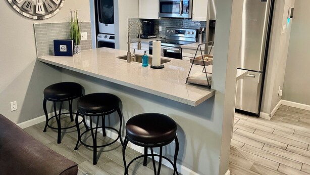 A modern kitchen with a central island, bar stools, stainless steel appliances, and a large wall clock. - AZ Peaceful Retreat in Scottsdale (Scottsdale)