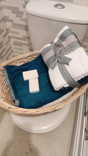 A wicker basket on a toilet containing a blue towel, a white towel, and two white soap bars. - Kirkcaldy, Fife • Lovely 2 Bedroom Flat • Sea View (Kirkcaldy)