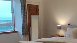 A bedroom with two beds, a window with a view, a wooden door, and a bedside lamp. - Kirkcaldy, Fife • Lovely 2 Bedroom Flat • Sea View (Kirkcaldy)