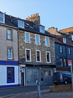 A multi-story building with stone and brick facades, a blue storefront, and a parked van. - Kirkcaldy, Fife • Lovely 2 Bedroom Flat • Sea View (Kirkcaldy)