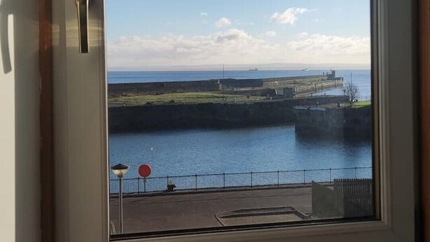 A window with a view of a coastal area, including a body of water and a distant shoreline. - Kirkcaldy, Fife • Lovely 2 Bedroom Flat • Sea View (Kirkcaldy)